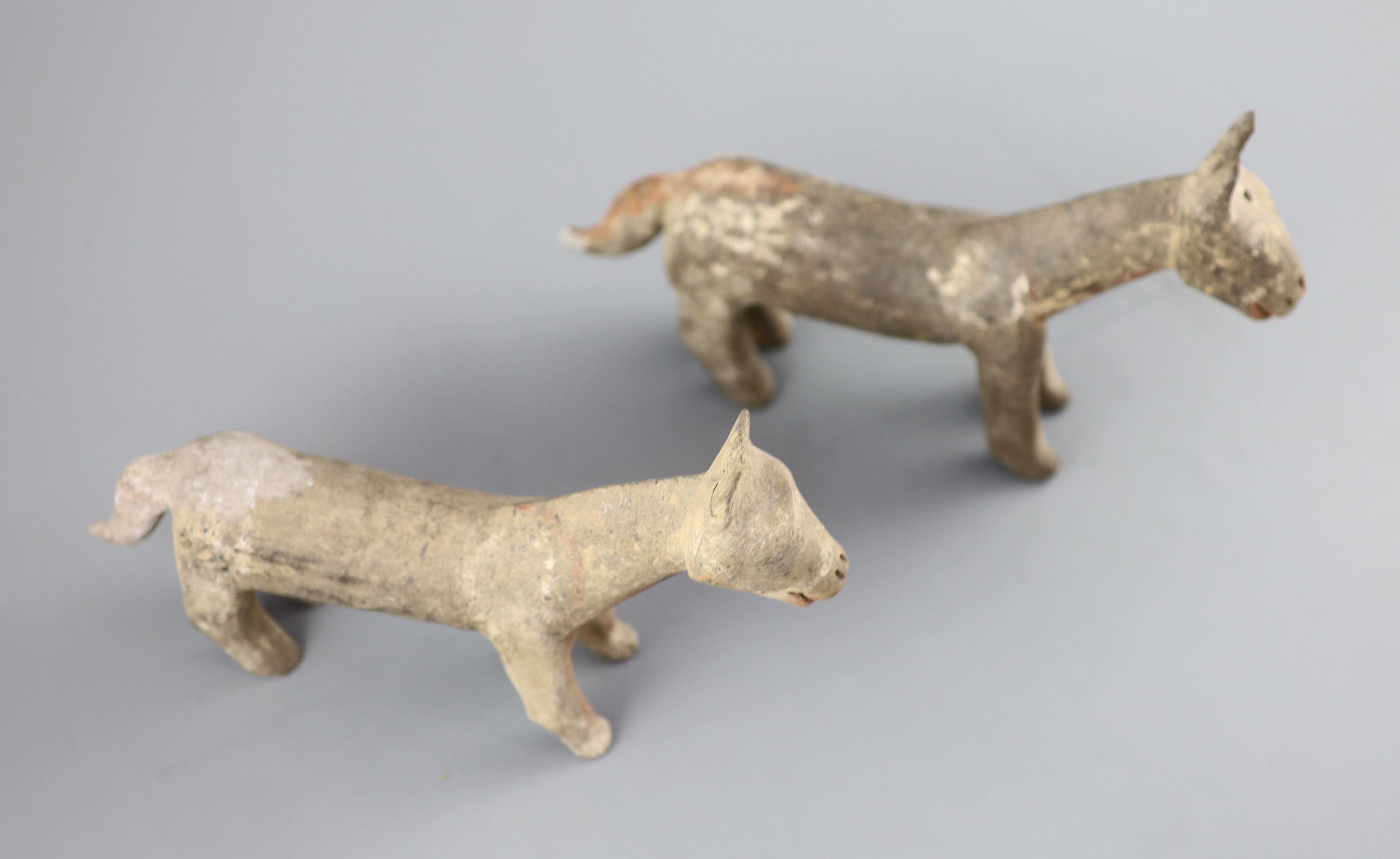 A pair of Chinese grey pottery models of dogs, Han dynasty or later, 26cm long, repairs